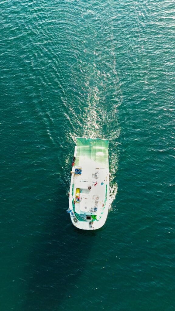 Aerial shot of a lone boat navigating calm blue waters, creating a serene wake.